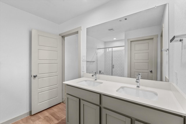 bathroom with a sink, double vanity, a stall shower, and wood finished floors