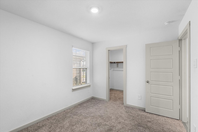 unfurnished bedroom with a spacious closet, carpet flooring, baseboards, and a closet
