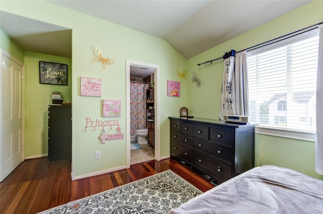 bedroom featuring wood finished floors, a spacious closet, vaulted ceiling, baseboards, and ensuite bath