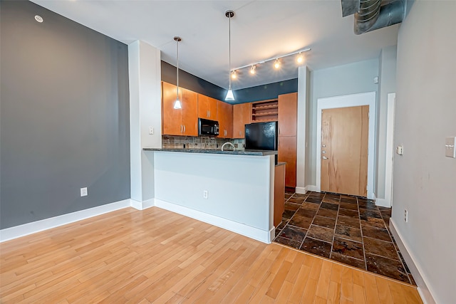 kitchen featuring kitchen peninsula, hanging light fixtures, backsplash, wood-type flooring, and black appliances