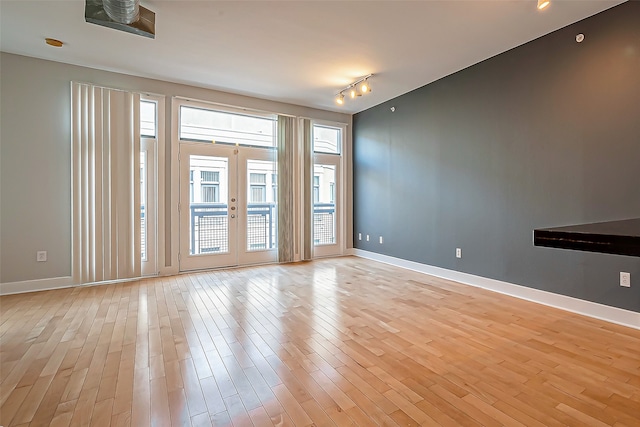 unfurnished living room featuring french doors, rail lighting, and light hardwood / wood-style floors