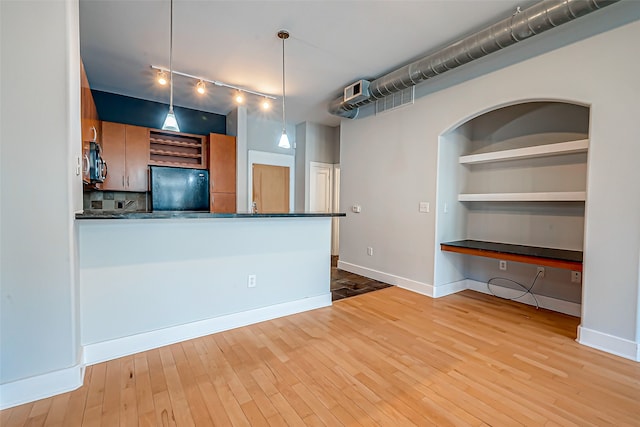 kitchen with black fridge, built in desk, light hardwood / wood-style flooring, hanging light fixtures, and rail lighting