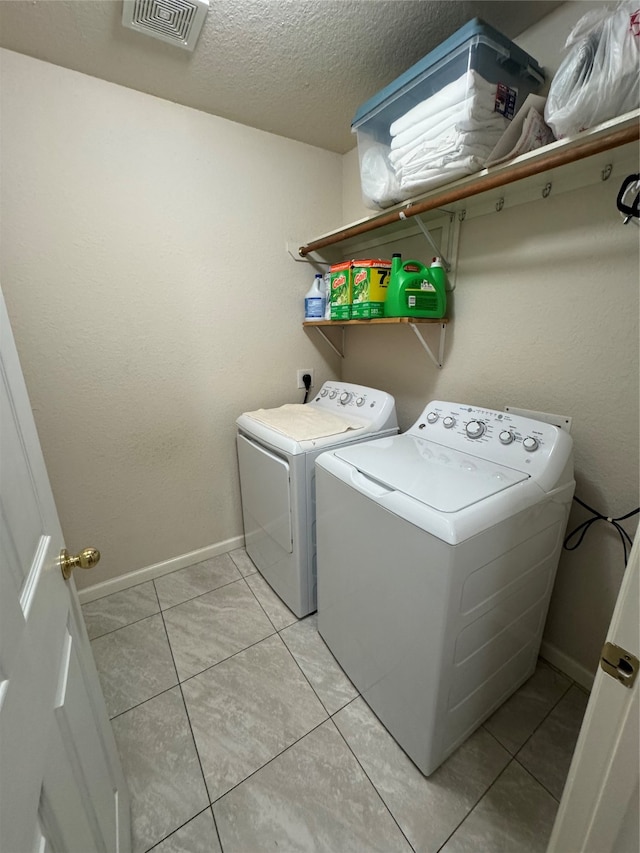 laundry area with a textured ceiling, light tile patterned floors, and washer and clothes dryer