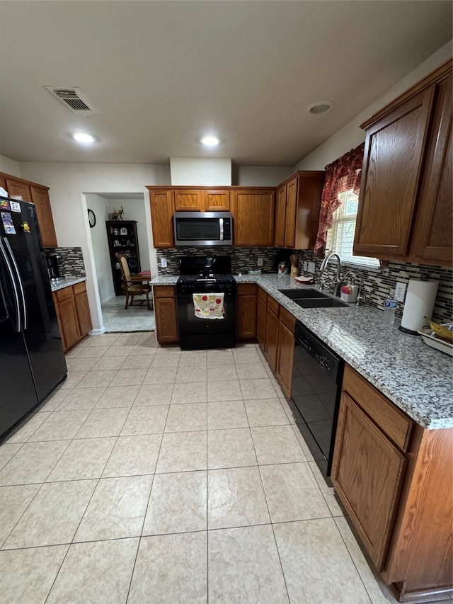 kitchen featuring tasteful backsplash, sink, light stone countertops, black appliances, and light tile patterned floors