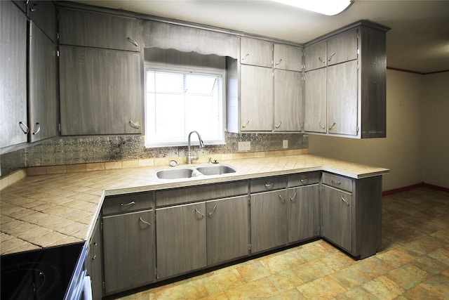 kitchen featuring stove, sink, tasteful backsplash, dark brown cabinets, and tile counters