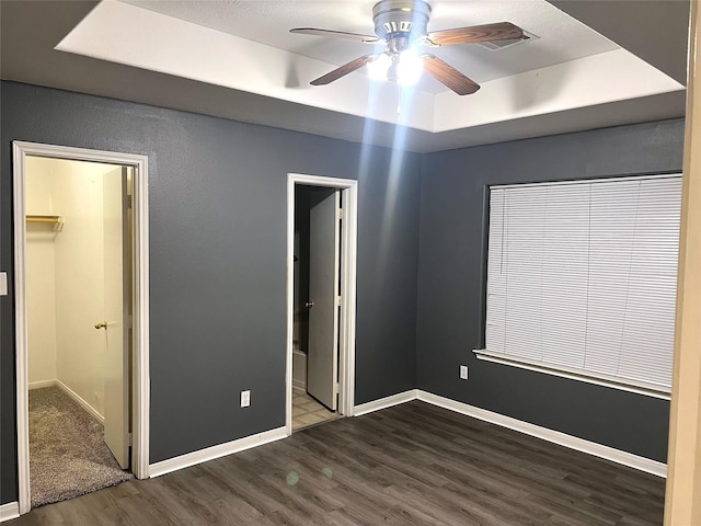 unfurnished bedroom with ceiling fan, a walk in closet, a tray ceiling, and hardwood / wood-style flooring