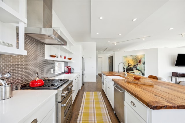 kitchen with wall chimney exhaust hood, wood-type flooring, butcher block counters, stainless steel appliances, and a large island