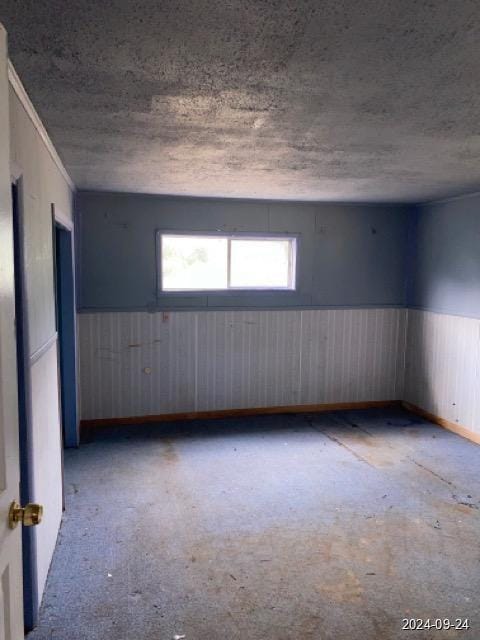 spare room featuring a textured ceiling and wainscoting
