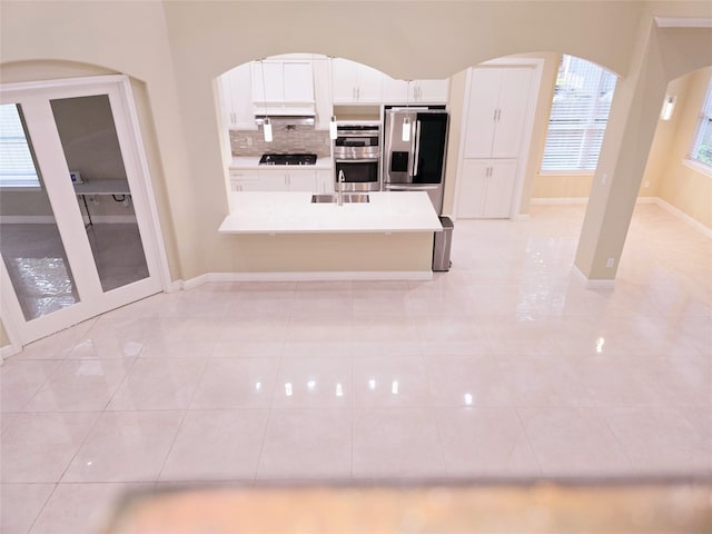 kitchen with light tile patterned flooring, kitchen peninsula, white cabinetry, appliances with stainless steel finishes, and decorative backsplash