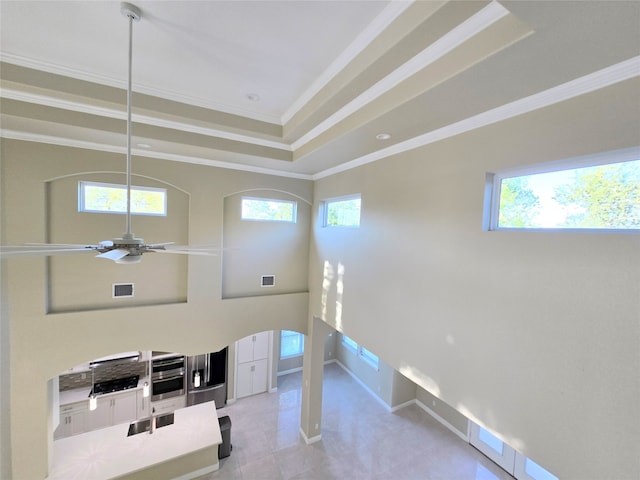 interior space with ceiling fan, a wealth of natural light, ornamental molding, and a raised ceiling