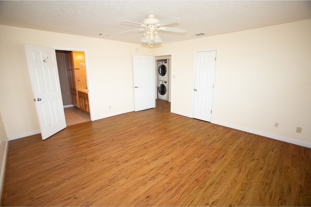 unfurnished bedroom with ceiling fan, a closet, wood-type flooring, ensuite bath, and stacked washer and clothes dryer