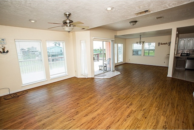 unfurnished living room with ceiling fan with notable chandelier, a healthy amount of sunlight, wood-type flooring, and a textured ceiling