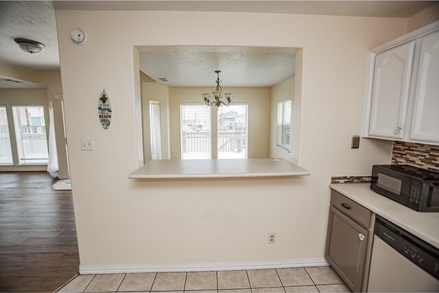 kitchen featuring stainless steel dishwasher, white cabinets, hanging light fixtures, an inviting chandelier, and light hardwood / wood-style flooring