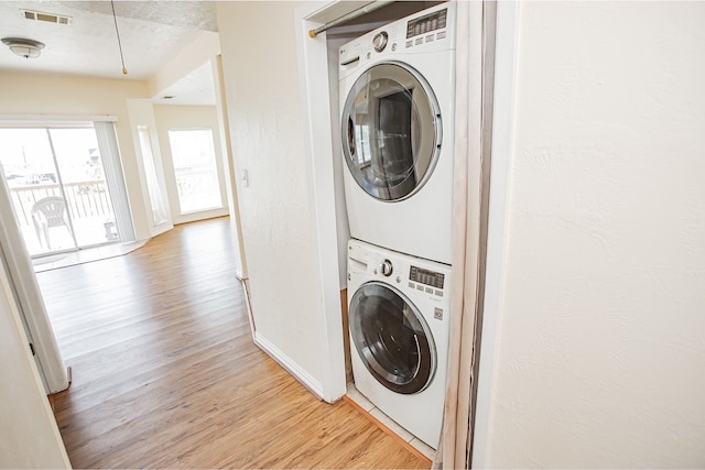 clothes washing area featuring stacked washing maching and dryer and light hardwood / wood-style flooring