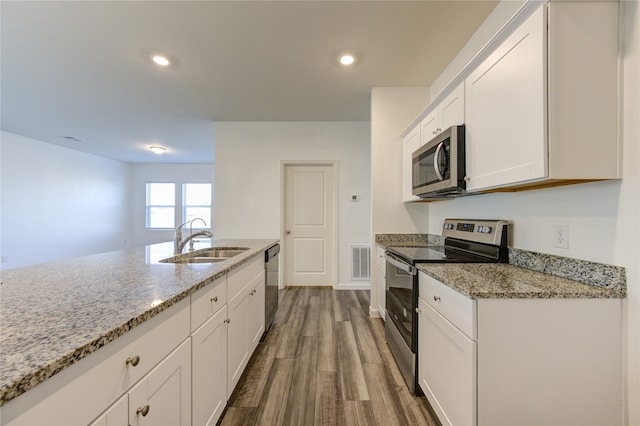 kitchen with sink, white cabinetry, stainless steel appliances, light stone countertops, and hardwood / wood-style floors