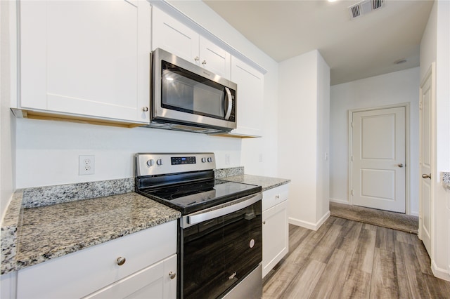 kitchen featuring stainless steel appliances, white cabinets, light stone counters, and light wood-type flooring