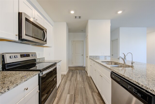 kitchen featuring stainless steel appliances, light stone countertops, light hardwood / wood-style flooring, and white cabinetry