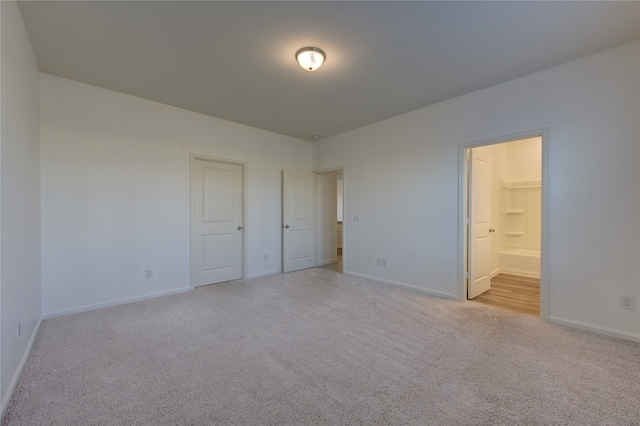 unfurnished bedroom with light carpet, ensuite bathroom, and a spacious closet