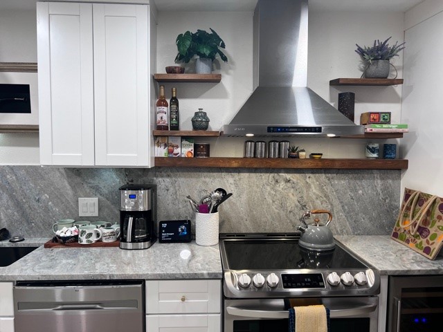 kitchen with light stone counters, white cabinets, wine cooler, wall chimney exhaust hood, and appliances with stainless steel finishes