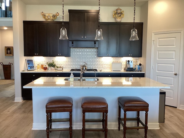 kitchen featuring an island with sink, light wood-type flooring, hanging light fixtures, and a kitchen breakfast bar