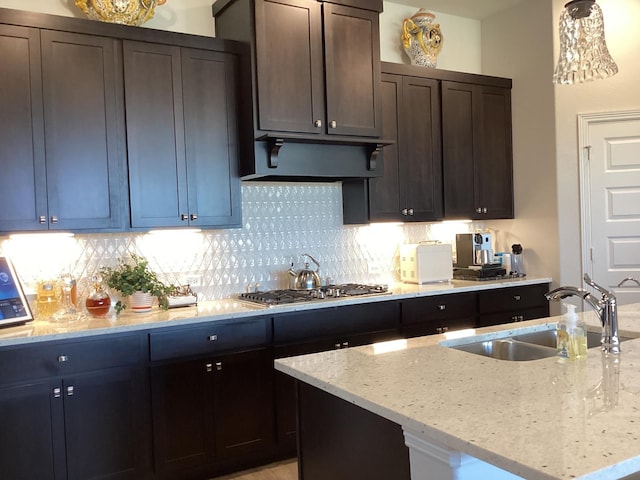 kitchen featuring dark brown cabinetry, a center island with sink, stainless steel gas stovetop, sink, and light stone countertops