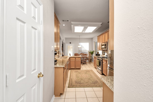 kitchen featuring pendant lighting, sink, light stone counters, appliances with stainless steel finishes, and light tile patterned floors