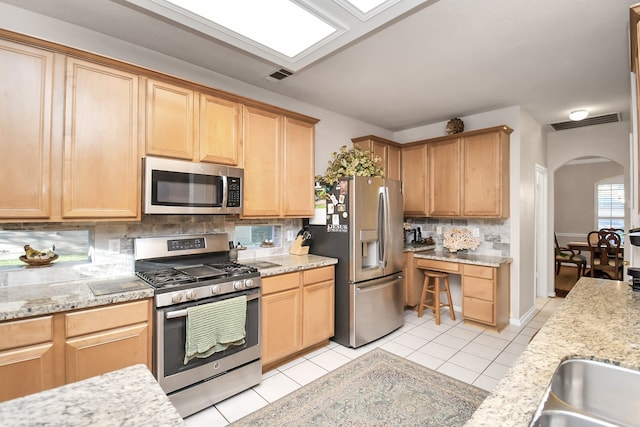 kitchen with light stone counters, light tile patterned flooring, appliances with stainless steel finishes, and tasteful backsplash