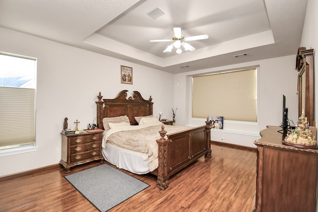 bedroom featuring a raised ceiling, dark hardwood / wood-style flooring, and ceiling fan