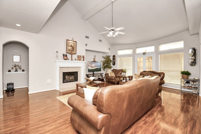 living room featuring ceiling fan, high vaulted ceiling, hardwood / wood-style floors, and a tile fireplace