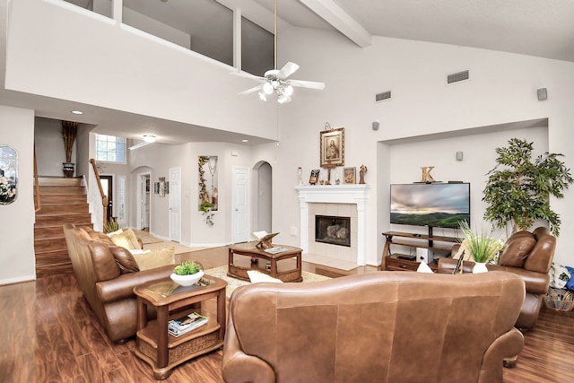 living room with ceiling fan, a tiled fireplace, wood-type flooring, beam ceiling, and high vaulted ceiling