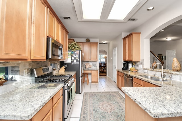 kitchen featuring light tile patterned flooring, sink, light stone counters, kitchen peninsula, and appliances with stainless steel finishes