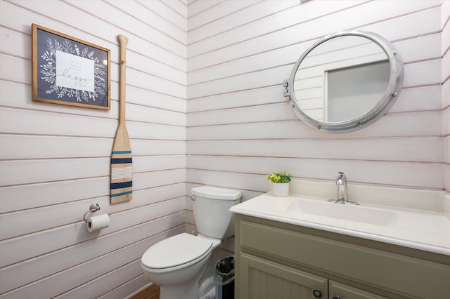 bathroom featuring wooden walls, toilet, and vanity