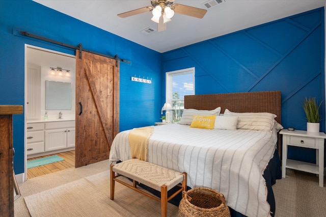 bedroom with a barn door, light hardwood / wood-style floors, ensuite bathroom, and ceiling fan