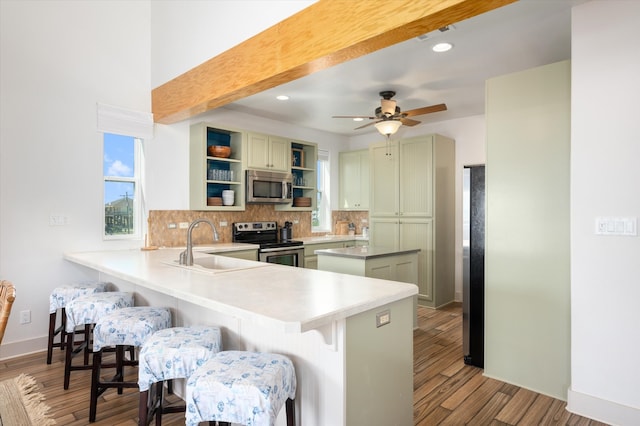 kitchen with wood-type flooring, green cabinets, sink, stainless steel appliances, and kitchen peninsula