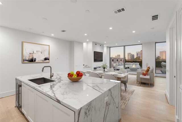 kitchen with light stone counters, sink, white cabinetry, and a kitchen island with sink