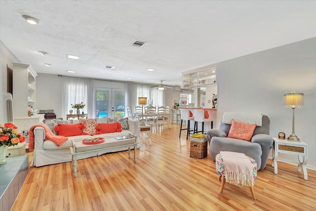 living room featuring ceiling fan, light hardwood / wood-style flooring, and a textured ceiling