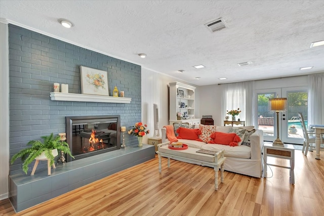 living room with a fireplace, brick wall, light wood-type flooring, and a textured ceiling