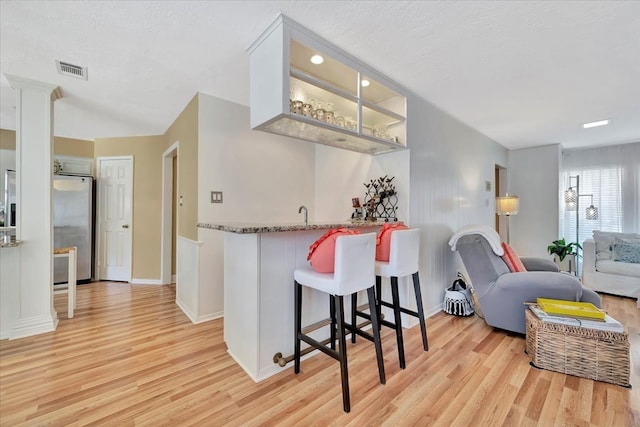 kitchen with stainless steel fridge, kitchen peninsula, stone countertops, a breakfast bar, and light wood-type flooring