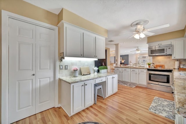 kitchen with light hardwood / wood-style flooring, decorative backsplash, light stone countertops, white cabinets, and appliances with stainless steel finishes