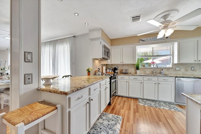 kitchen with light stone counters, white cabinets, sink, appliances with stainless steel finishes, and decorative backsplash