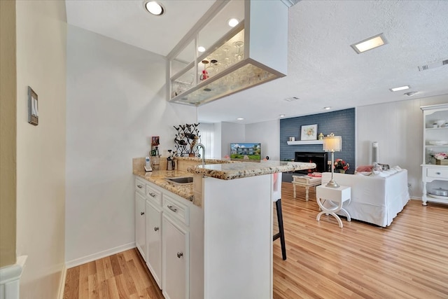 kitchen featuring light wood-type flooring, a breakfast bar area, kitchen peninsula, white cabinets, and a textured ceiling