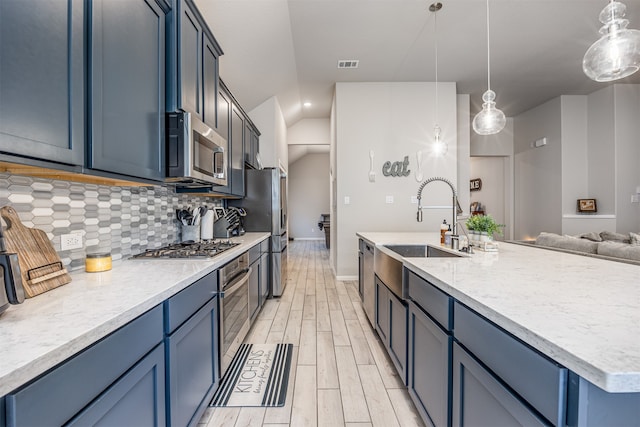 kitchen with decorative backsplash, a kitchen island with sink, sink, hanging light fixtures, and appliances with stainless steel finishes