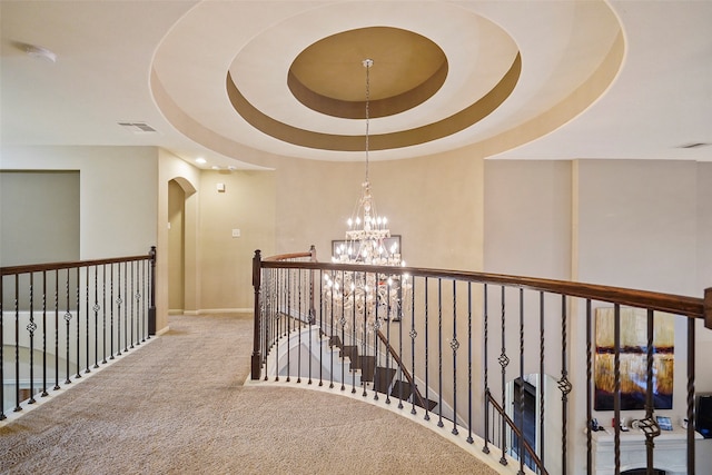 hall featuring a tray ceiling, carpet, and an inviting chandelier