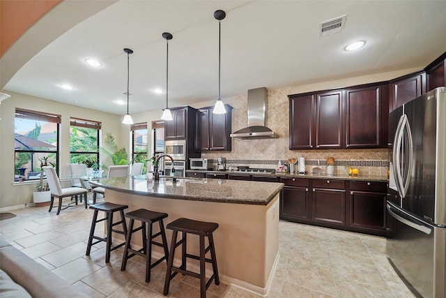 kitchen featuring sink, hanging light fixtures, wall chimney exhaust hood, an island with sink, and appliances with stainless steel finishes