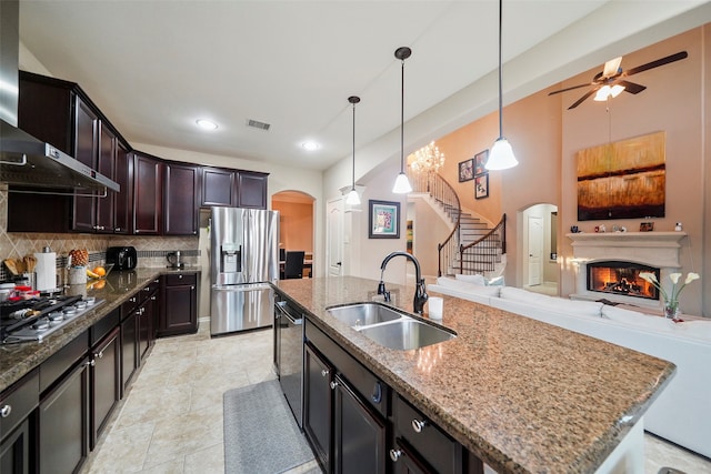 kitchen with tasteful backsplash, wall chimney exhaust hood, stainless steel appliances, sink, and an island with sink