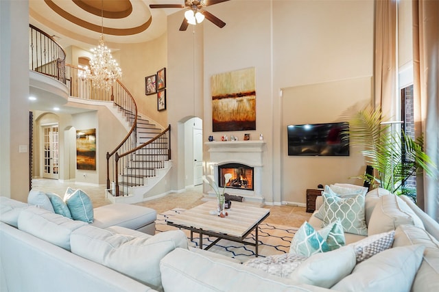 living room with ceiling fan with notable chandelier, a high ceiling, and a tray ceiling