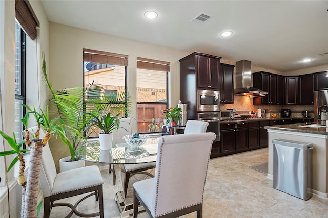 kitchen featuring decorative backsplash, a wealth of natural light, wall chimney range hood, and appliances with stainless steel finishes