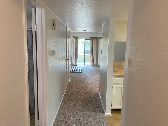 hallway with a textured ceiling and light colored carpet