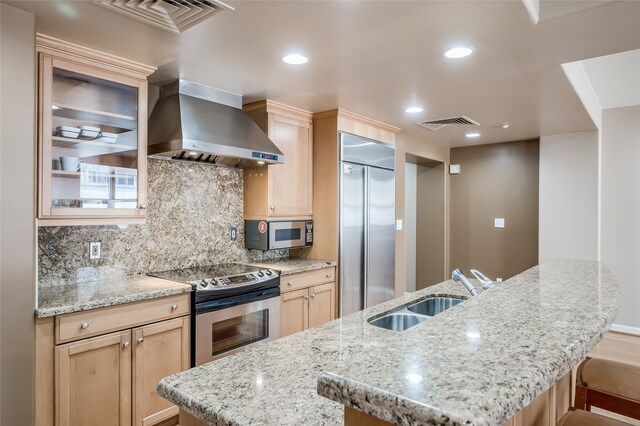 kitchen featuring light brown cabinets, stainless steel appliances, sink, and wall chimney range hood