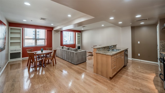 kitchen featuring an island with sink, light wood-type flooring, sink, stainless steel dishwasher, and light stone countertops